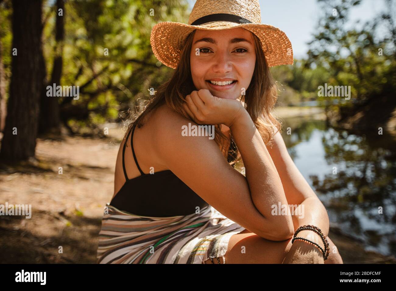 Portrait of beautiful woman in bikini wearing a hat sitting by the lake. Female relaxing near a