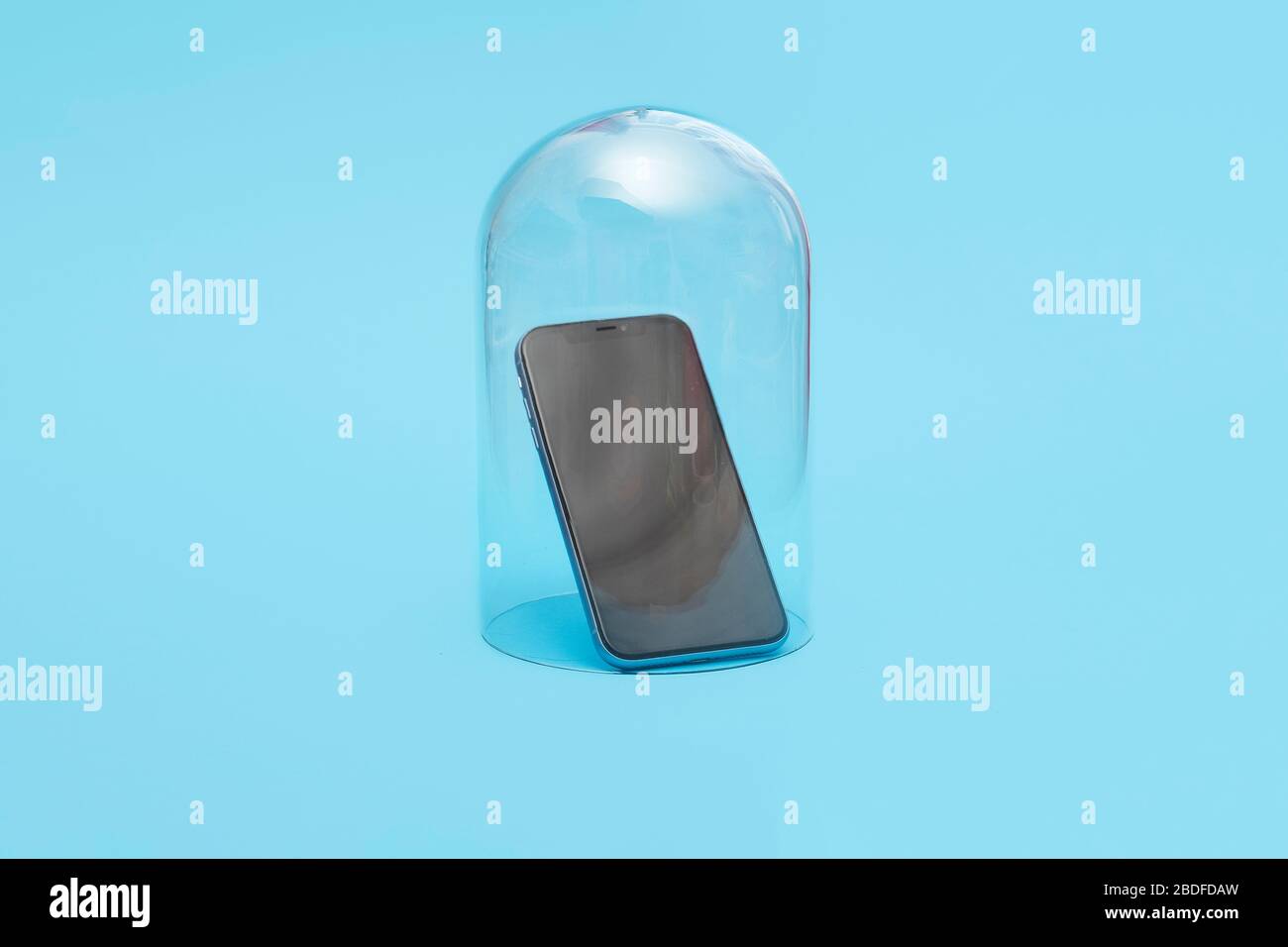 Mobile smartphone in quarantine under a glass cloche dome on a blue background with copy space and room for text Stock Photo