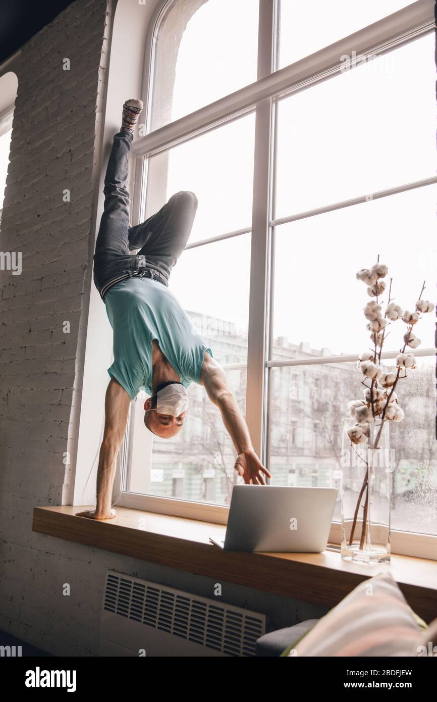 Inspired. Young man doing yoga at home while being quarantine and freelance online working. Remote office, isolated. Concept of healthy lifestyle, wellness, being safe while coronavirus pandemic. Stock Photo