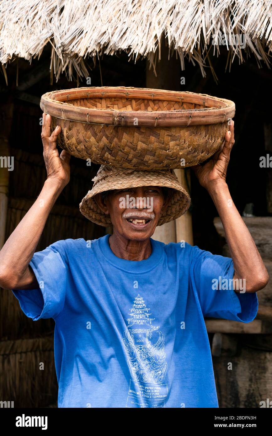 Vertical portrait of a traditional seasalt maker carrying a basket on his head in Bali, Indonesia. Stock Photo