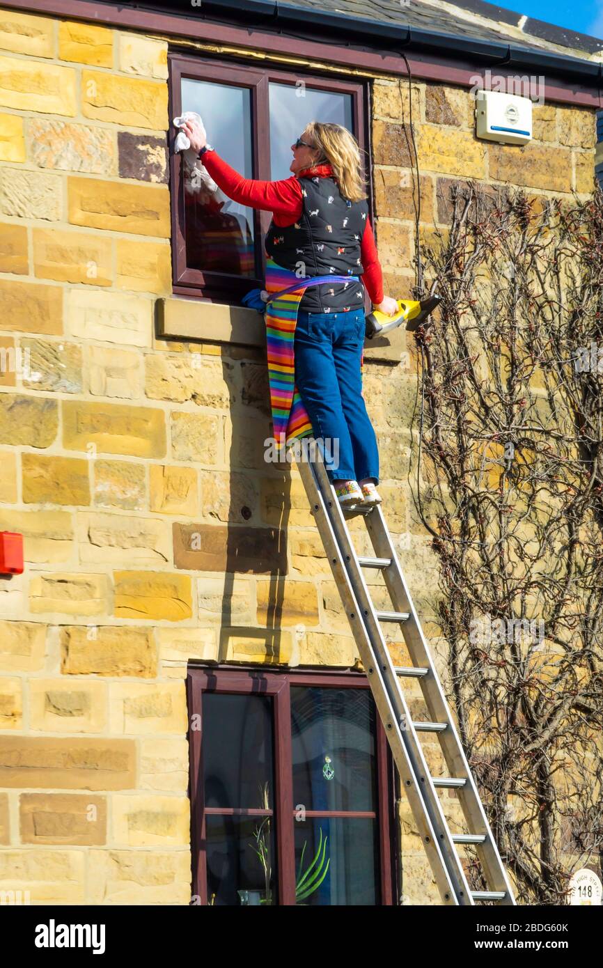 White woman on a tall ladder cleaning house windows on an upper floor Stock Photo