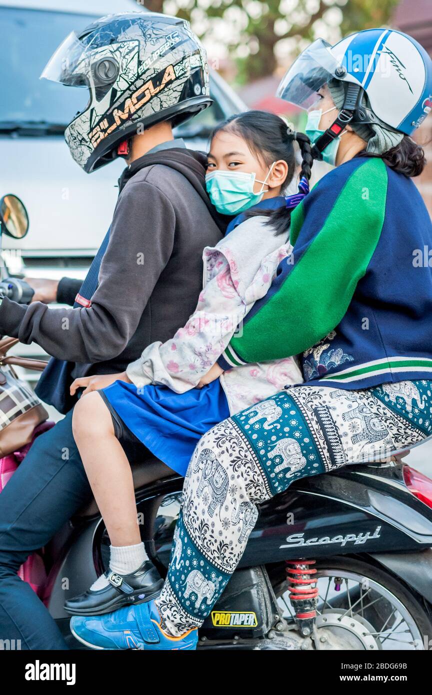 A young Thai schoolgirl is picked up from school and taken through the streets of Chiang Mai Thailand on a motorbike. Stock Photo