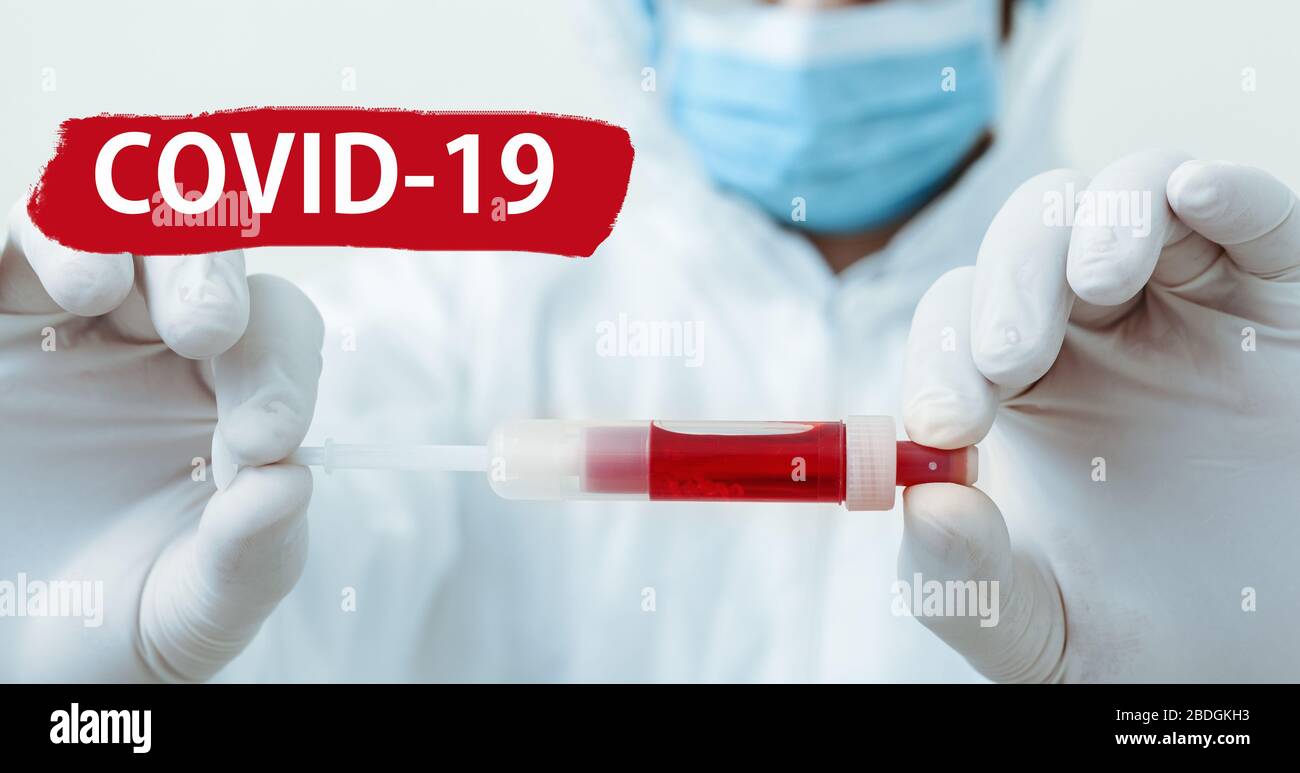 Text covid-19 on red warning sign. Coronavirus blood test in doctors hands. Doctor in protective medical suit, biological hazard, mask on white Stock Photo