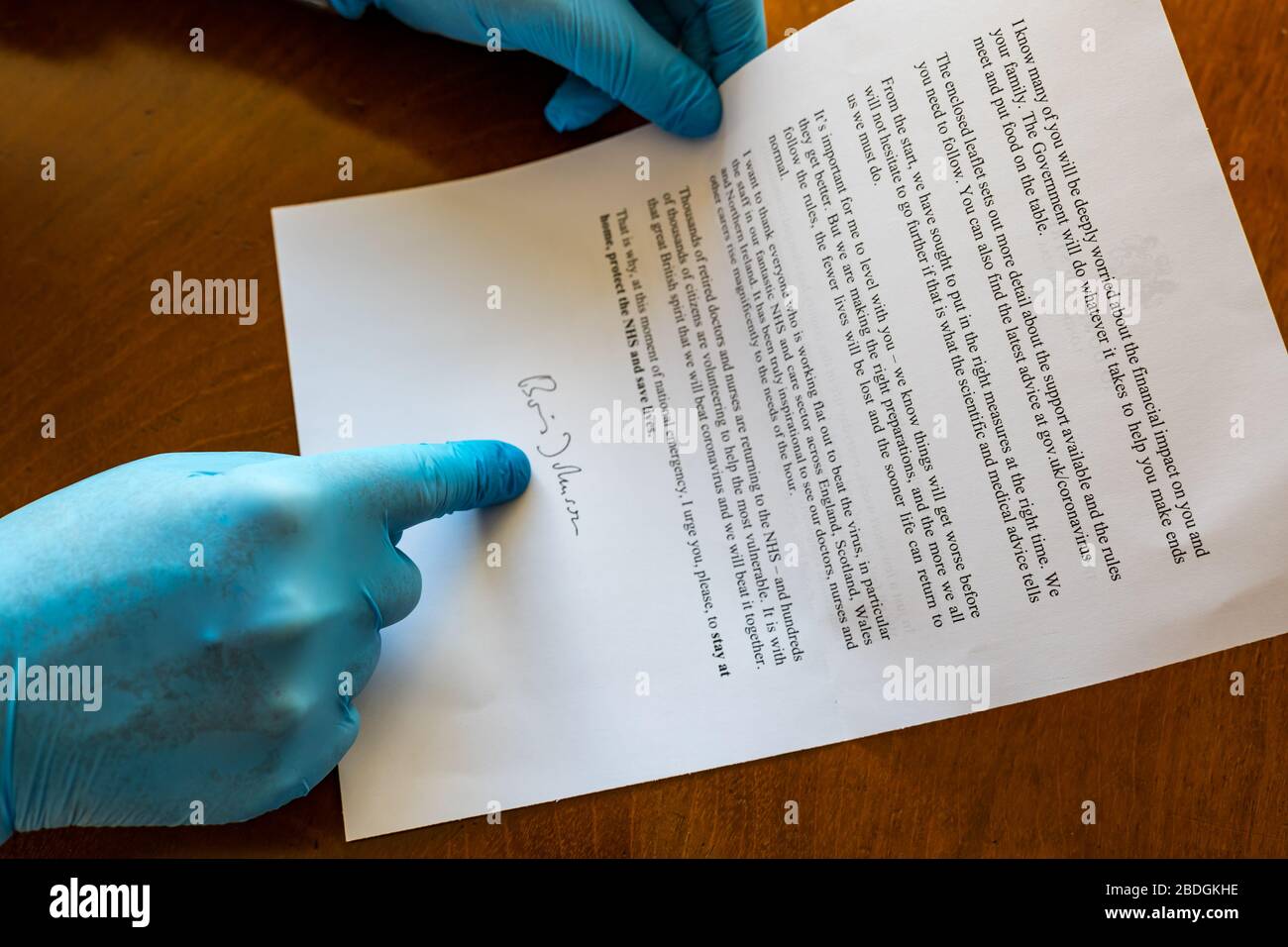 Man wearing surgical gloves holding HM Government letter with Boris Johnson signature about Covid-19 Coronavirus, United Kingdom Stock Photo