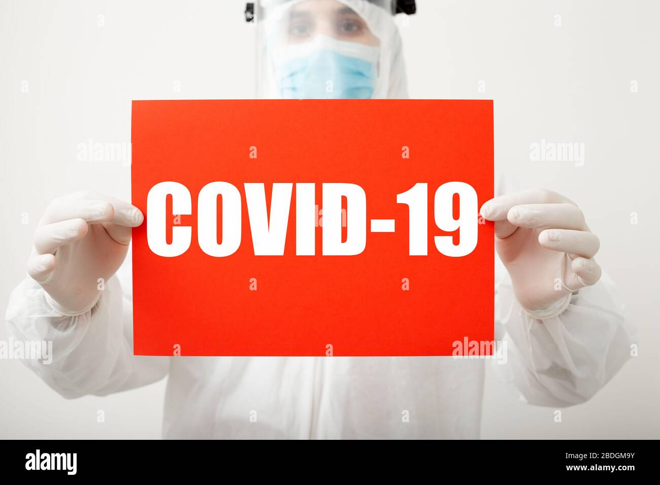 Text covid-19 on red warning sign in doctors hands. Coronavirus protection. Doctor in protective medical suit, biological hazard, mask on white Stock Photo