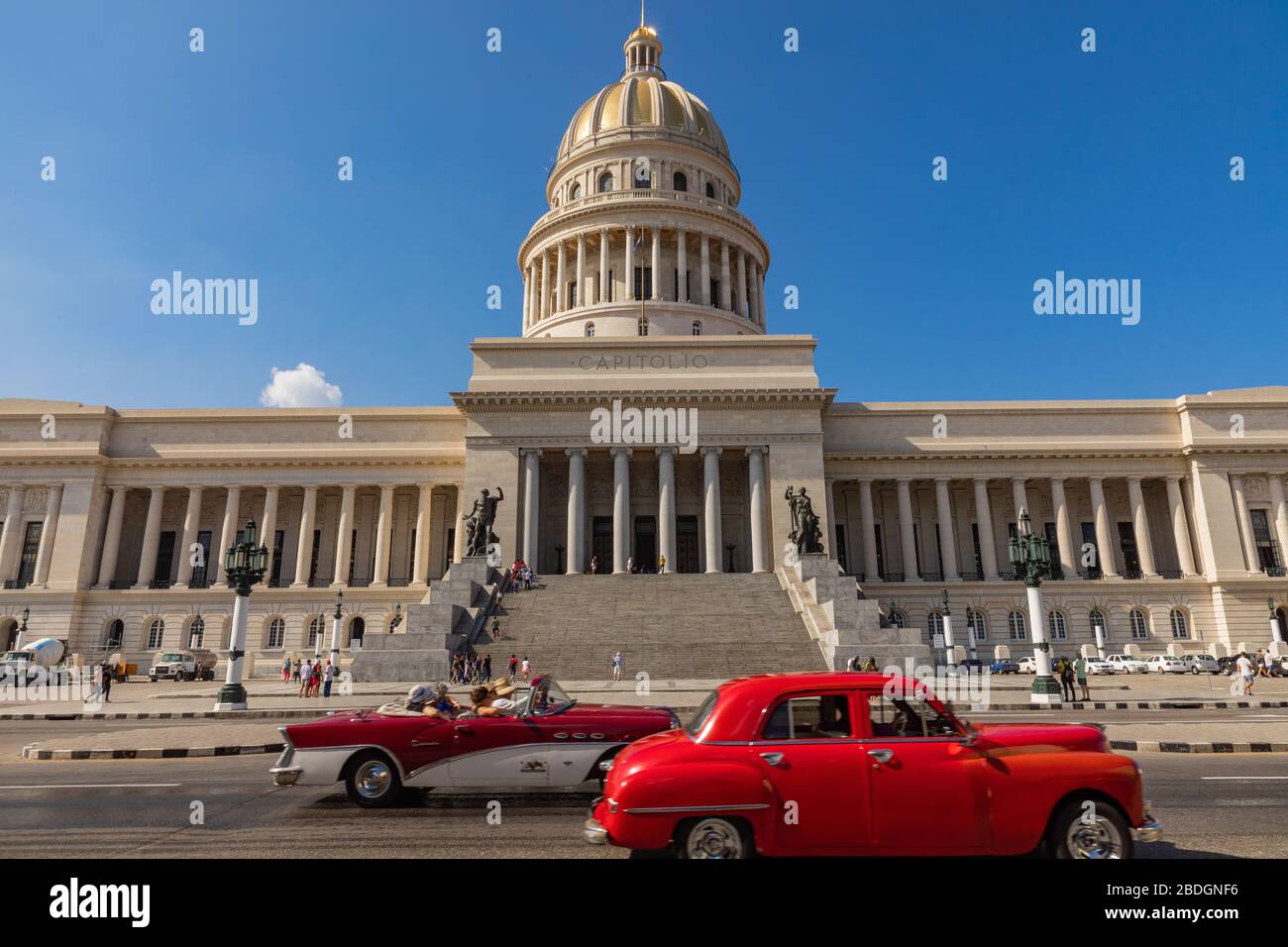 HAVANA, CUBA - DECEMBER 10, 2019: Brightly colored classic American cars serving as taxis pass on the main street in front of the Capitolio building i Stock Photo