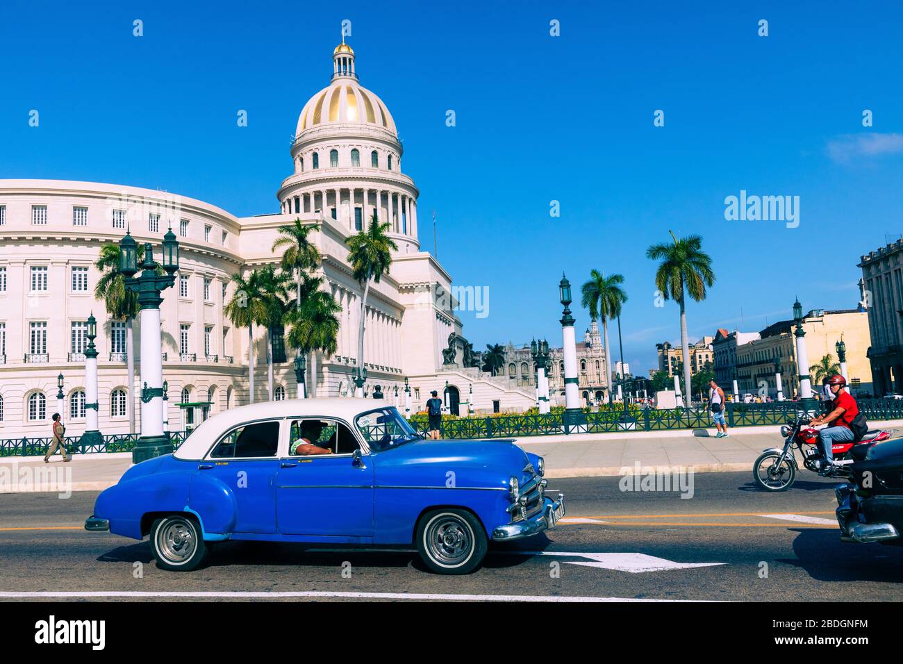 HAVANA, CUBA - DECEMBER 10, 2019: Brightly colored classic American cars serving as taxis pass on the main street in front of the Capitolio building i Stock Photo