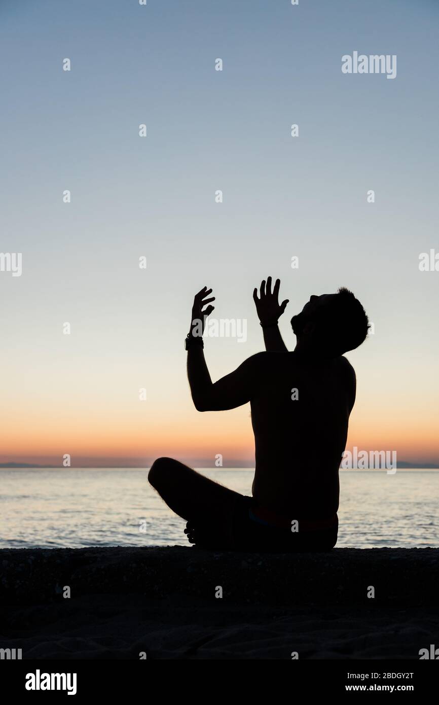 Silhouette of a man praying to God on the beach in sunset Stock Photo