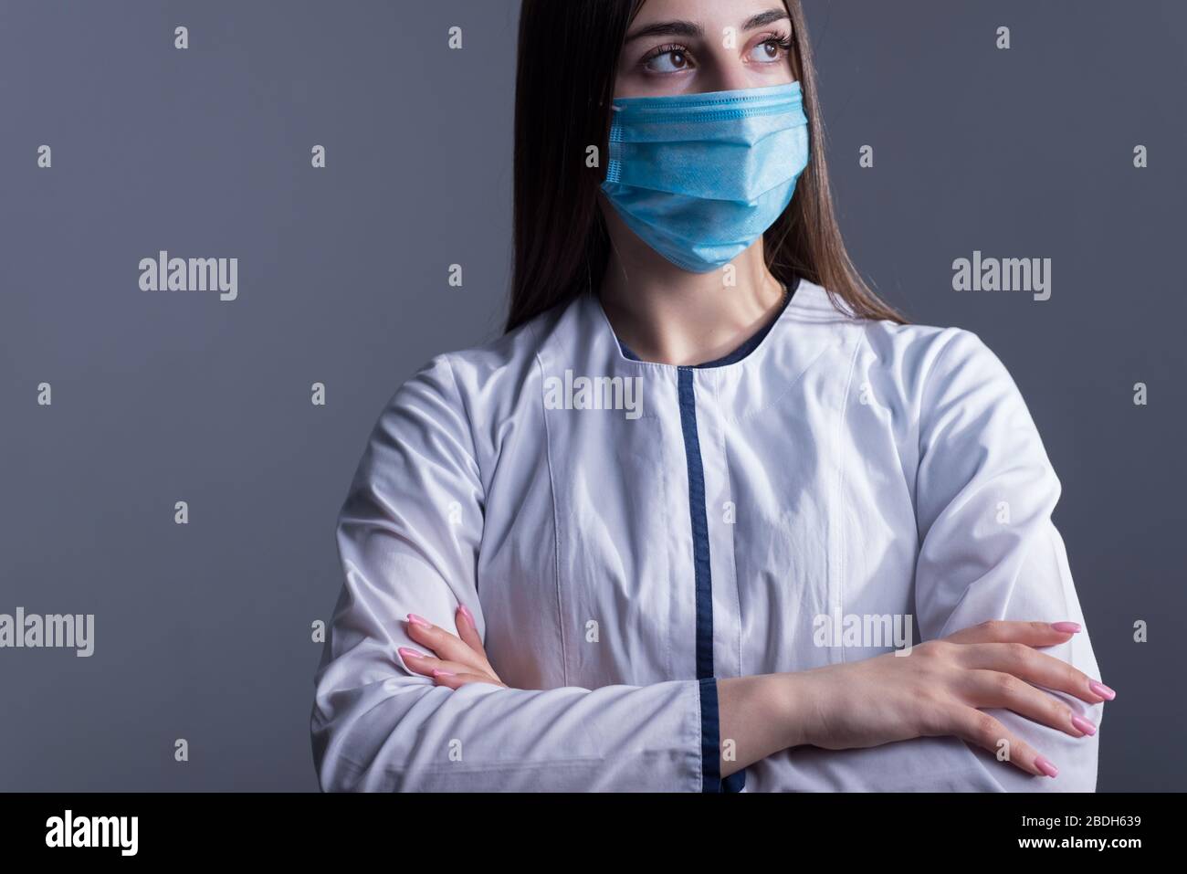 Closeup portrait of a young girl. doctor in a white coat, and a medical mask. looking at the camera. Studio photo on a gray background. Precautions wh Stock Photo