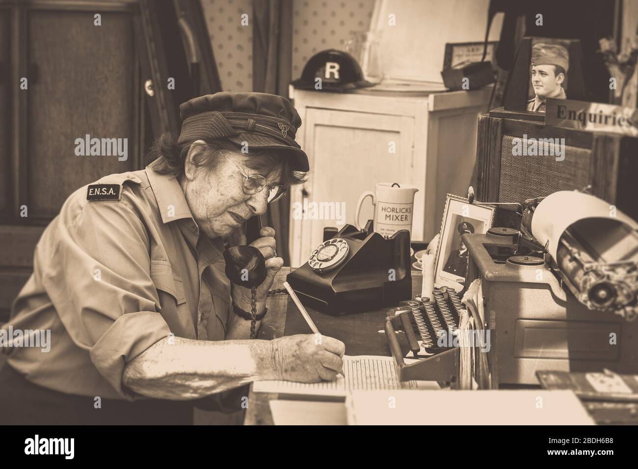 Old-fashioned sepia side view of senior woman in uniform working isolated in vintage office, Severn Valley Railway, 1940s wartime summer event, UK. Stock Photo