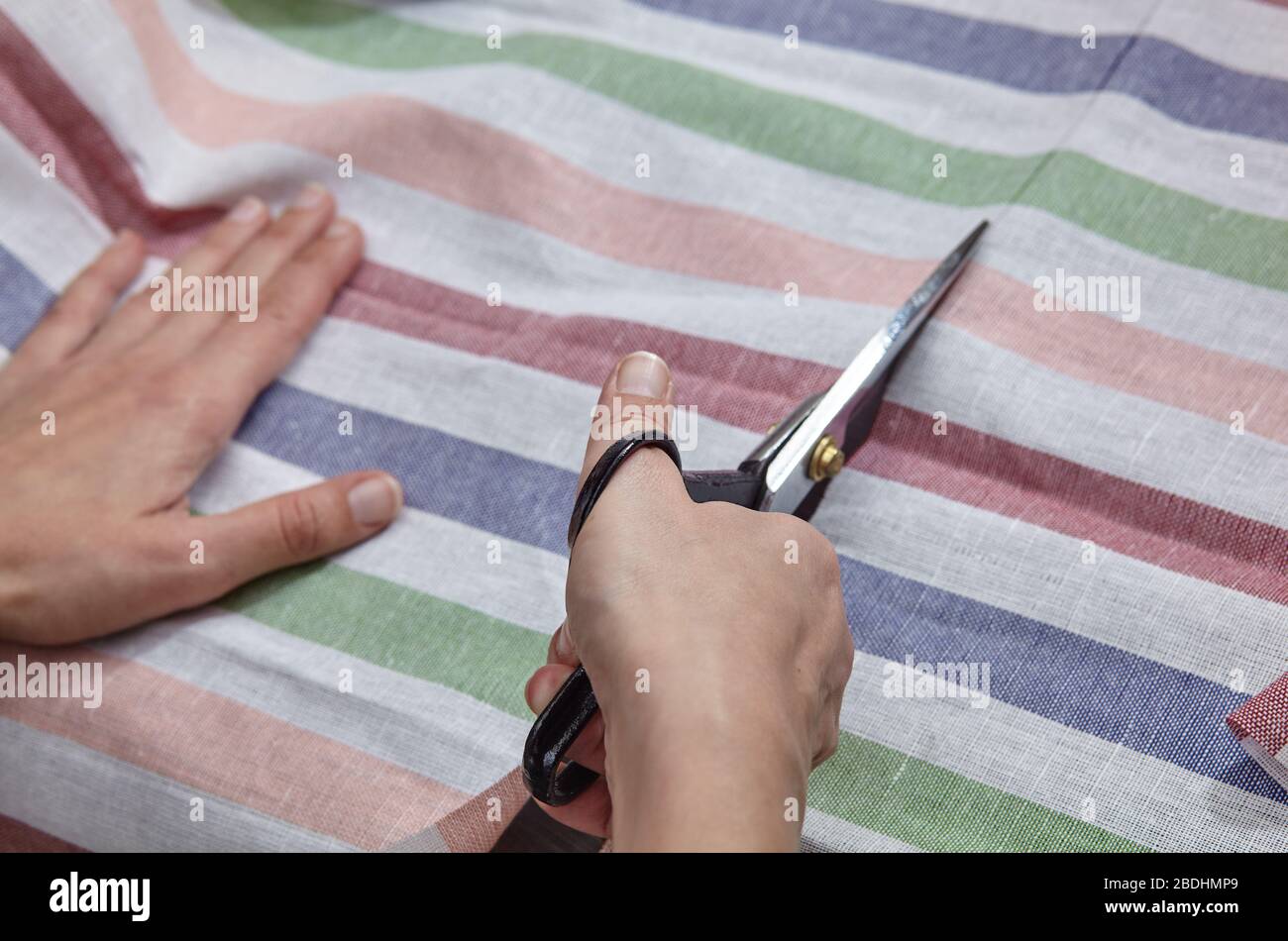 Tailor girl cuts striped fabric cloth with scissors Stock Photo