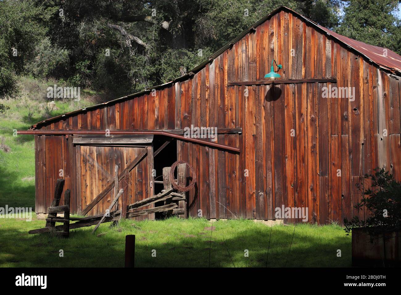 Old redwood barn, built with hand hewn redwood planks in the 1880's, in sunlight, some green grass, in the Daley Ranch Preserve, Escondido, California Stock Photo