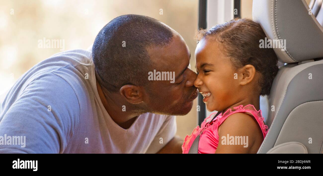Affectionate father kissing his young daughter on the cheek sitting in the backseat of a car Stock Photo