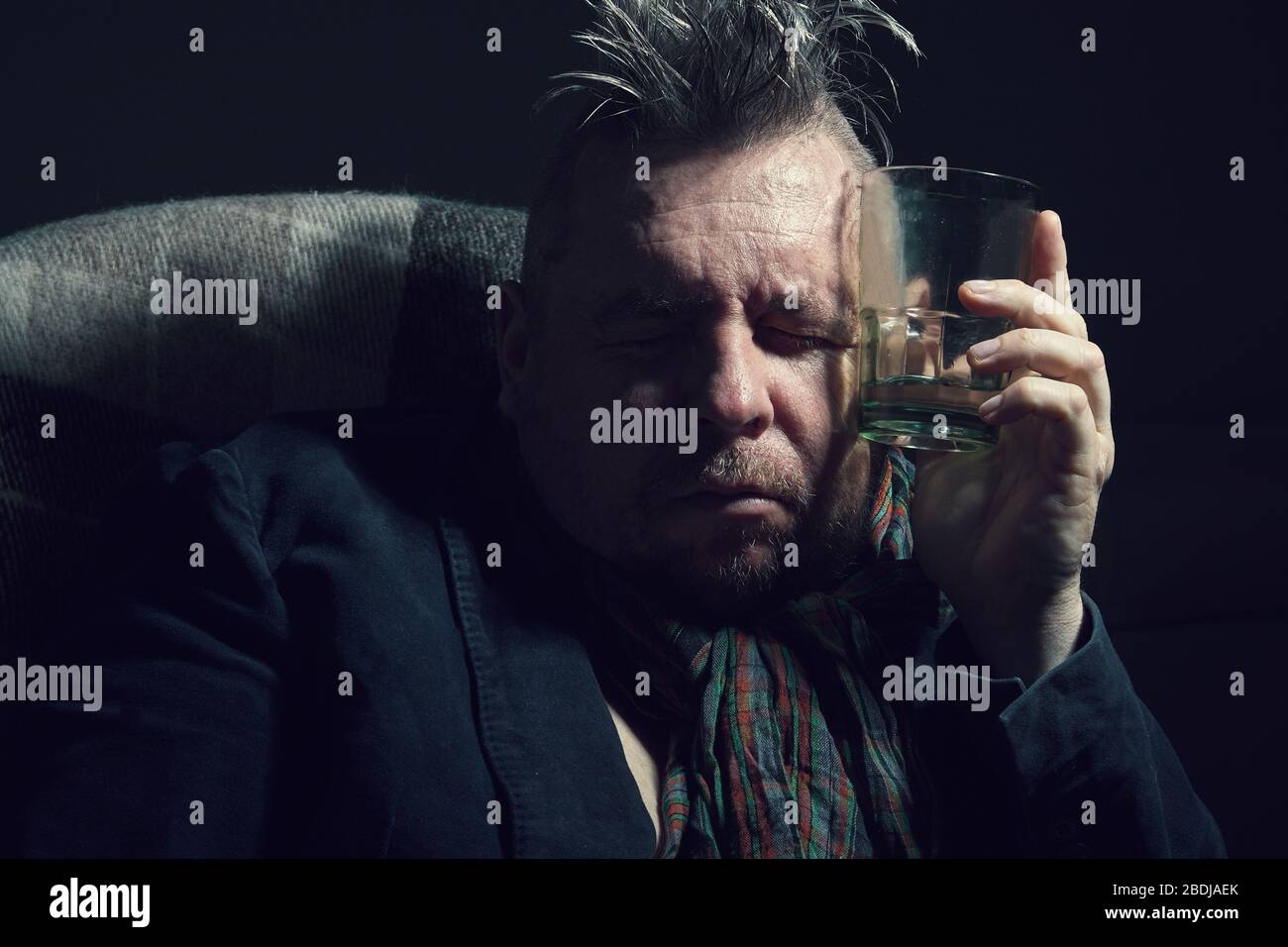 A man in depression is sitting with a glass of alcohol in his hand Stock Photo