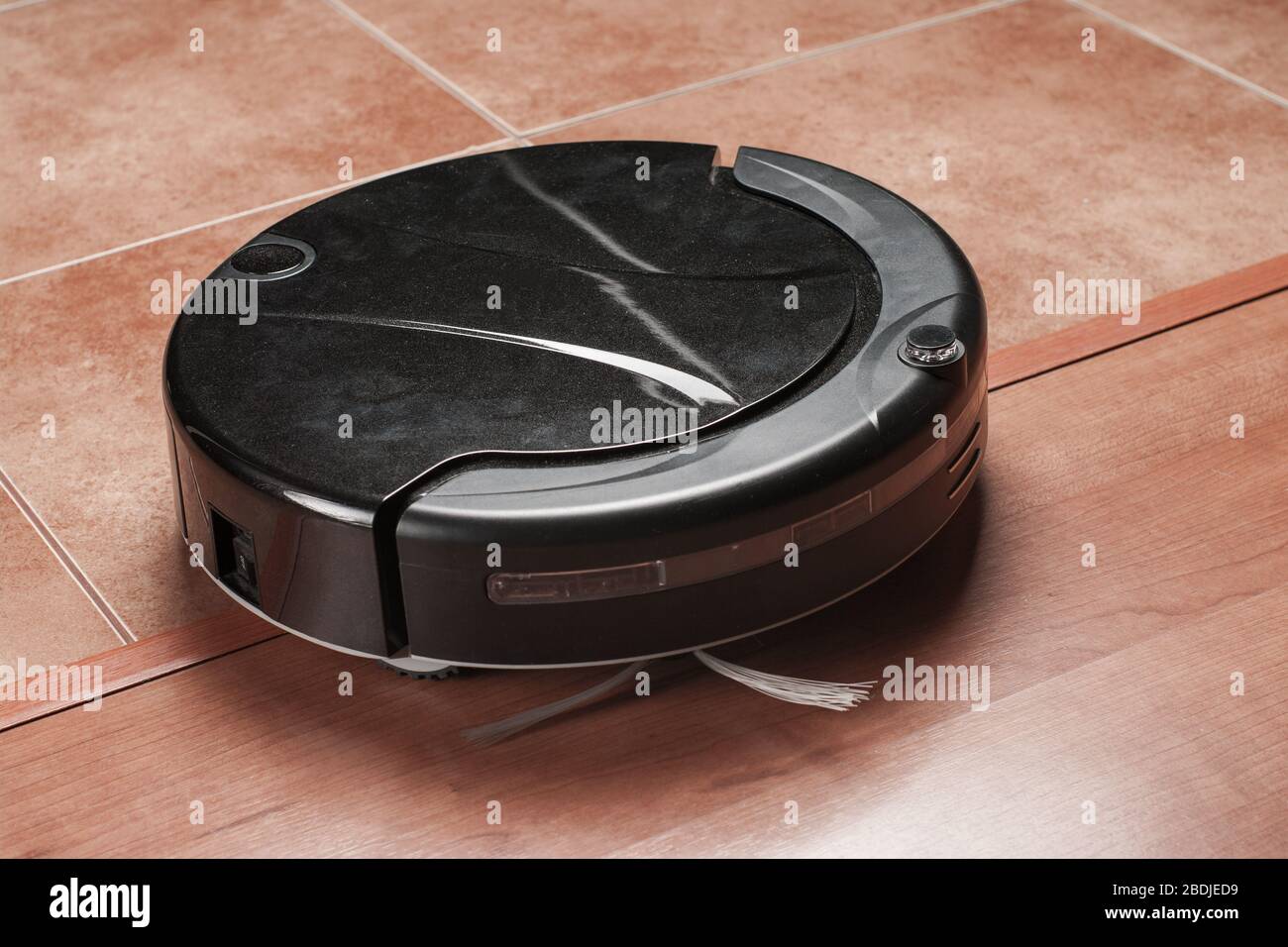 black robotic vacuum cleaner crosses threshold between laminate and tile floor. The robot is
