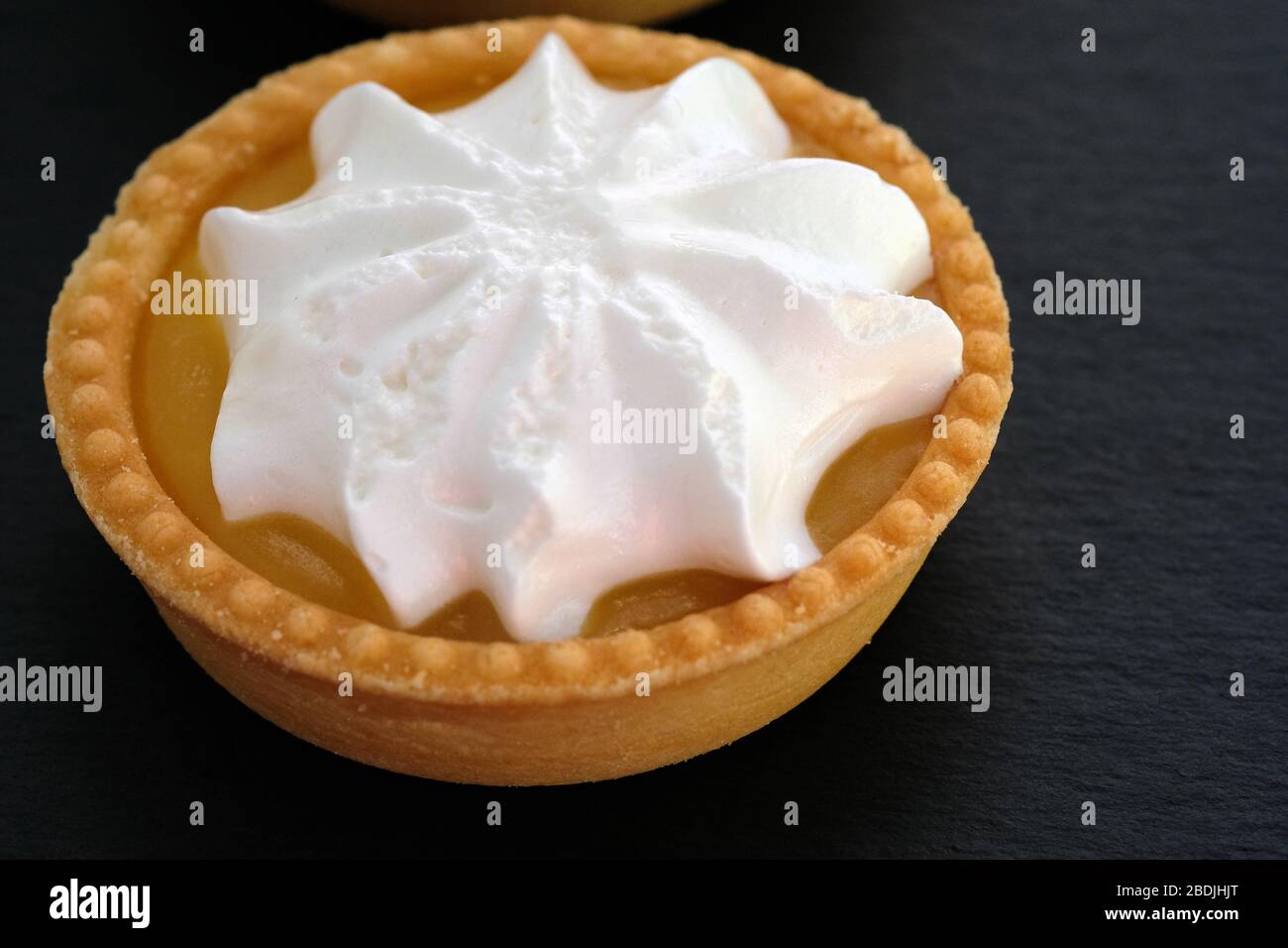 Tartlet with lemon cream and whipped squirrels. Round cake on a shortcrust pastry. Shortcrust tartlet and whipped cream on a black background. Stock Photo