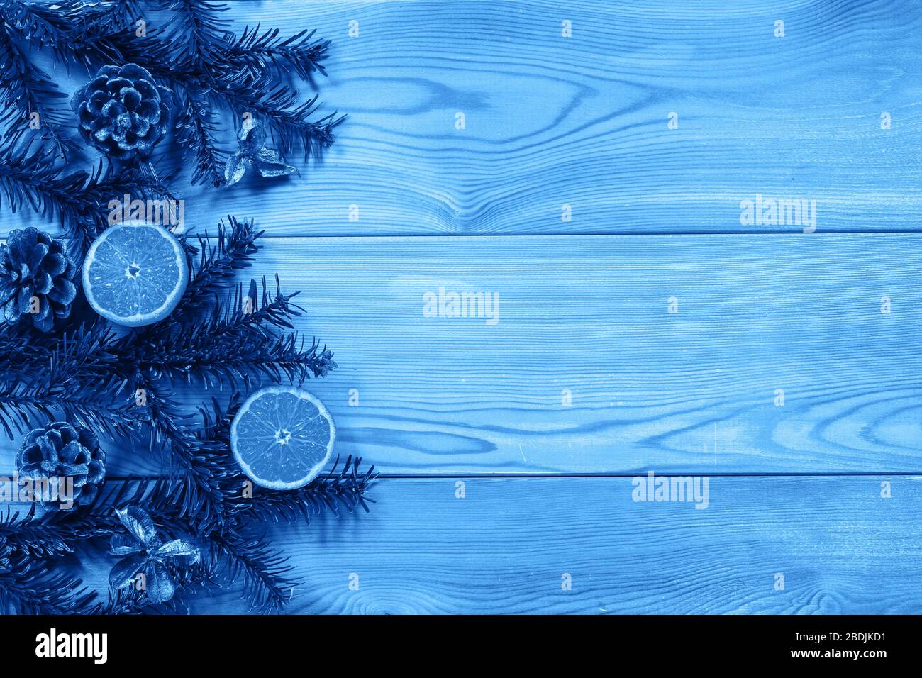 Green fir branches with pine cones and juicy cut tangerines on the edge of a textured wooden table. Tinting in Classic Blue. Space for text Stock Photo