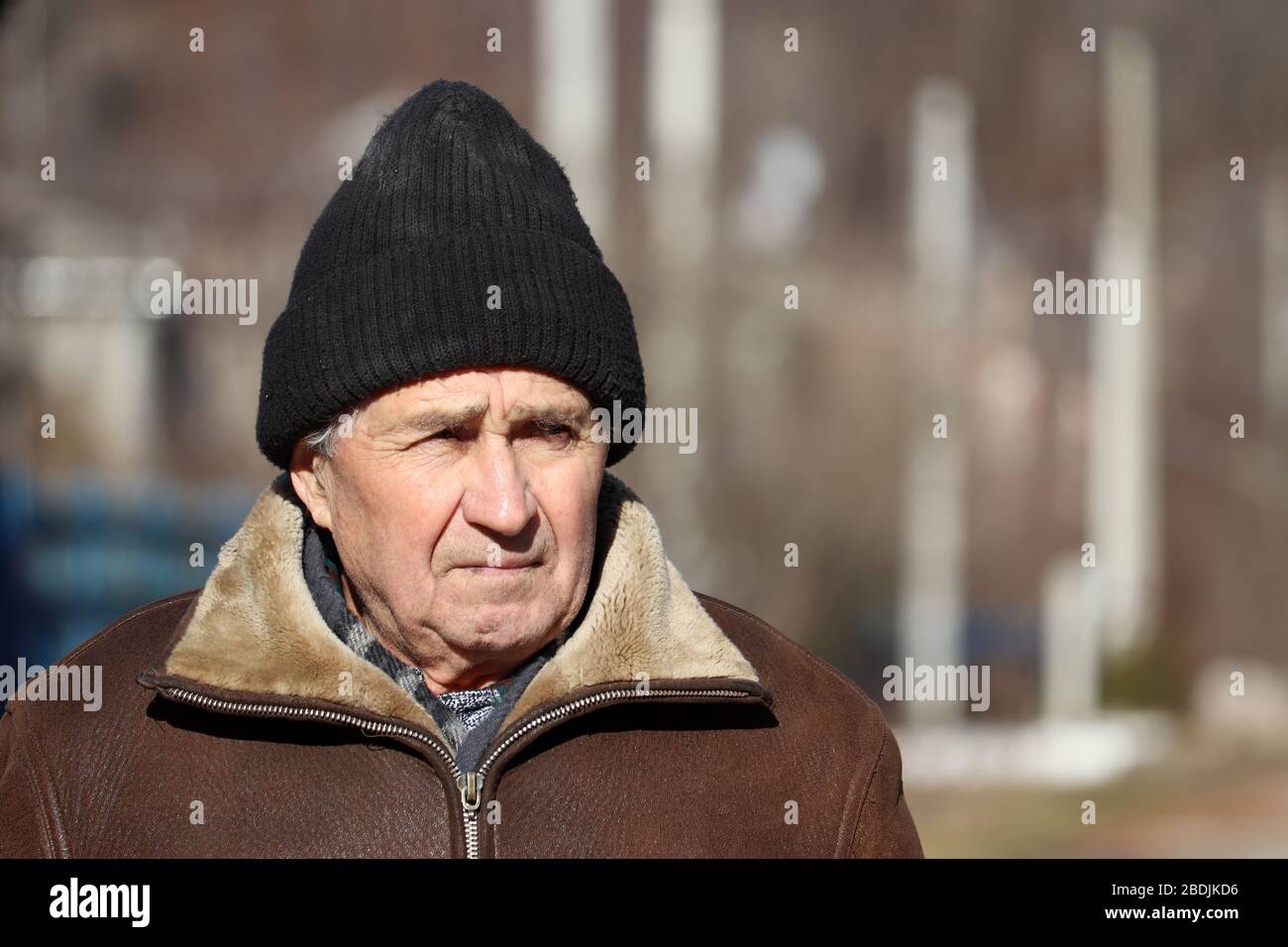 Elderly man standing on rural background in sunny spring day. Sad face expression, concept of walking during coronavirus quarantine, life in village Stock Photo
