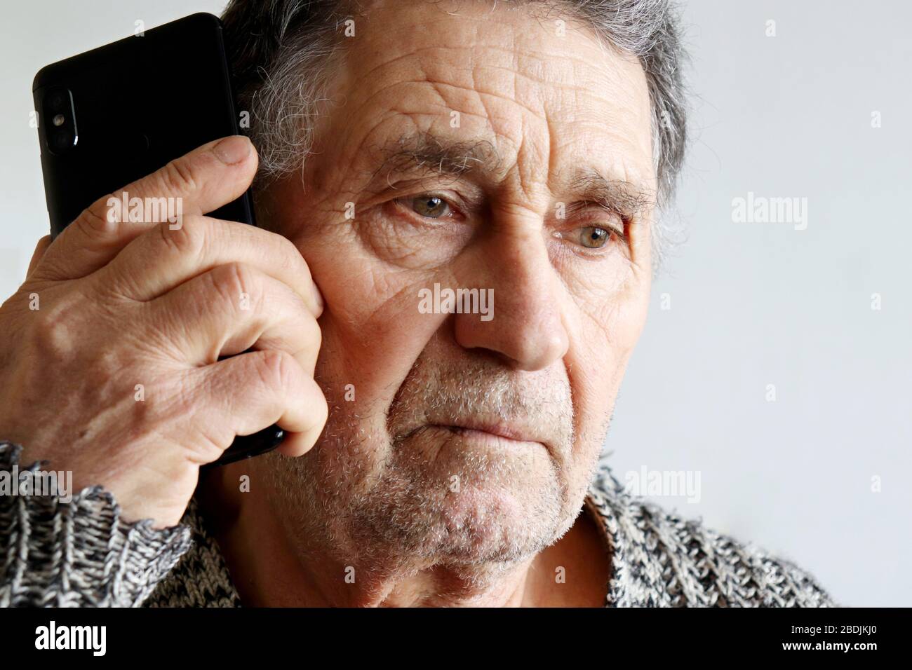 Portrait of unshaven elderly man talking on mobile phone, smartphone in male hands close up. Concept of communication in retirement Stock Photo