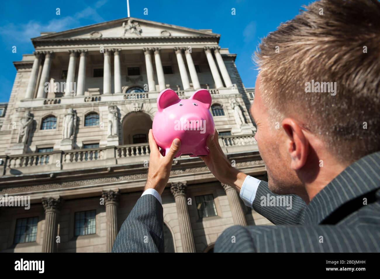 Businessman holding a bright pink piggy bank outside the traditional ...
