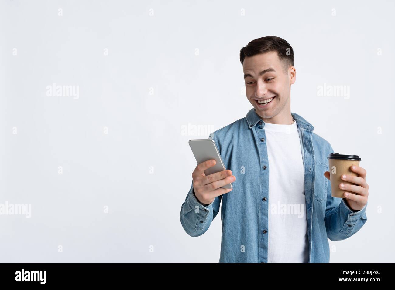 Guy is looking at smartphone, holding cup Stock Photo