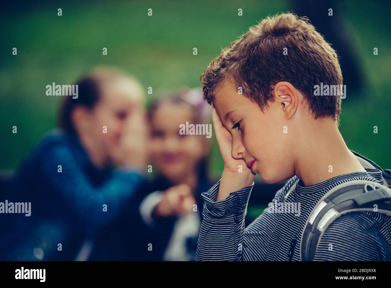 Little sad boy feeling left out, teased and bullied by his classmates. Unhappy boy having problems fitting in with others at school. Stock Photo