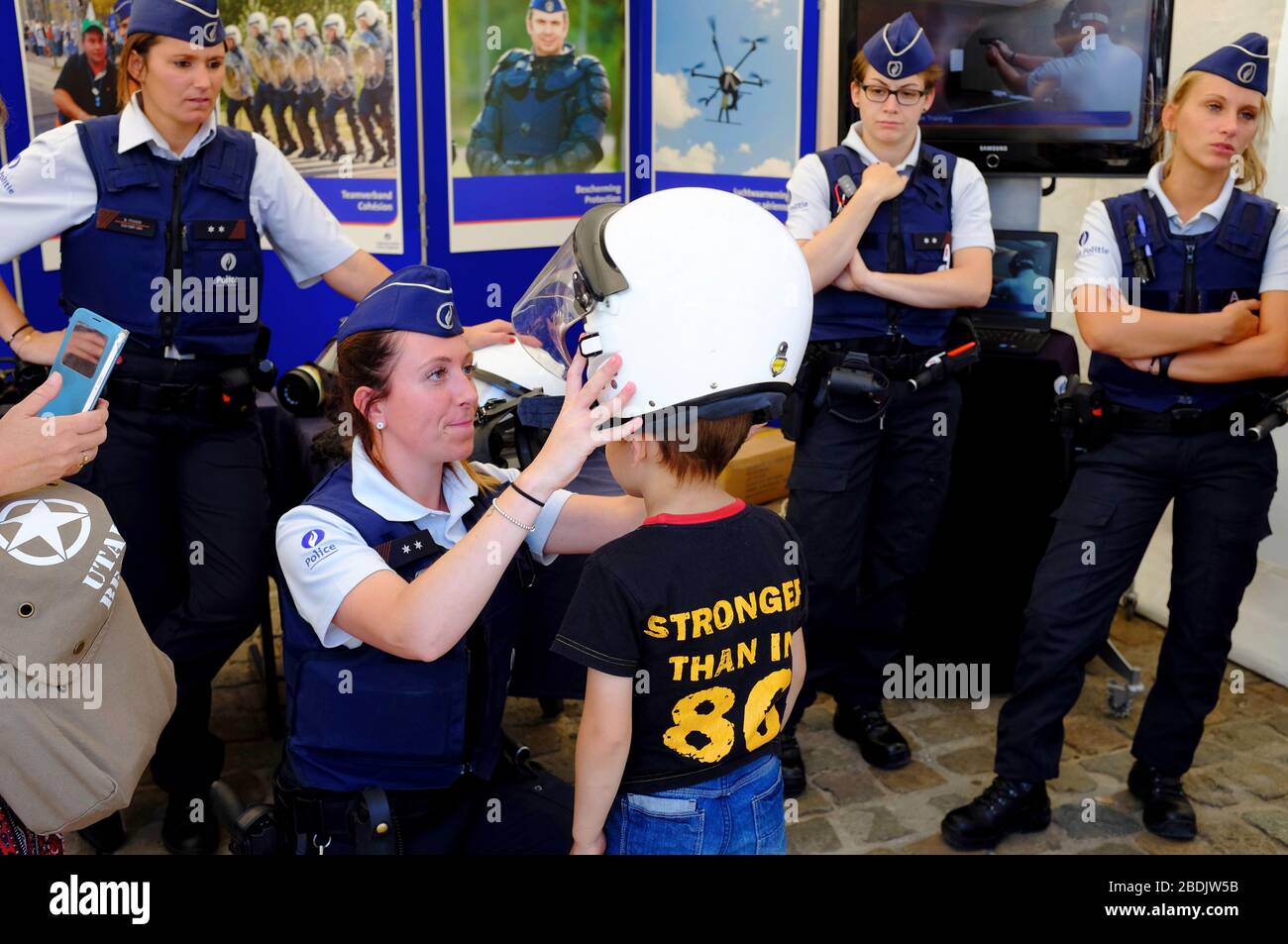 A female police officer help a child trying out a police helmet in the Police force and law enforcement show exhibition during Belgian National Day celebration.Brussels.Belgium Stock Photo