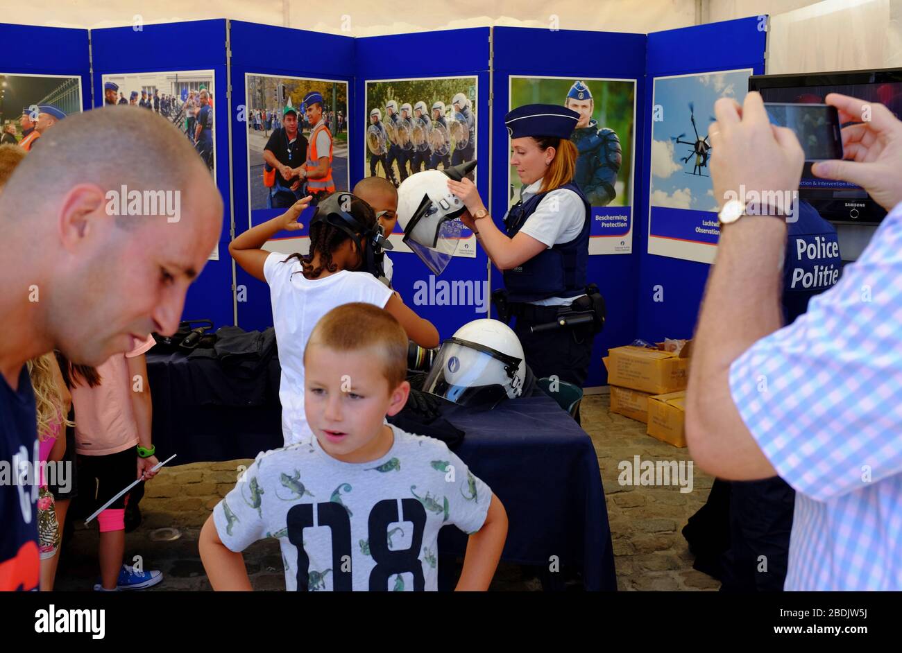 Police and law enforcement show as a part of Belgian National Day celebration with a female police officer help children trying out police helmet in the background.Brussels.Belgium Stock Photo
