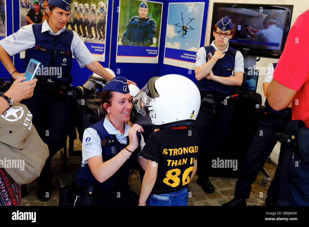 A female police officer help a child trying out a police helmet in the Police force and law enforcement show exhibition during Belgian National Day celebration.Brussels.Belgium Stock Photo