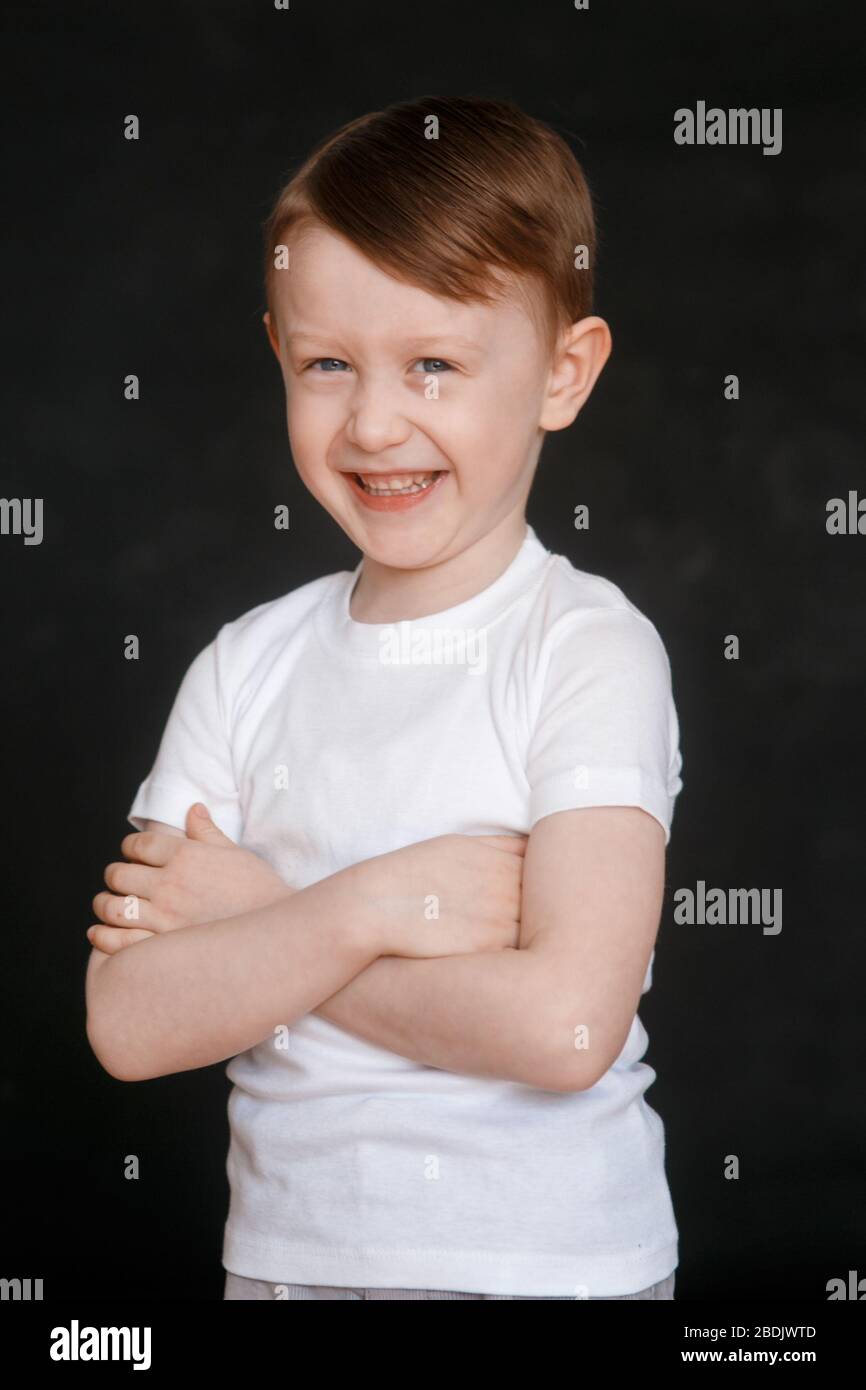 a cheerful 5 year old boy in a white t shirt on a black background smiles looking at the camera