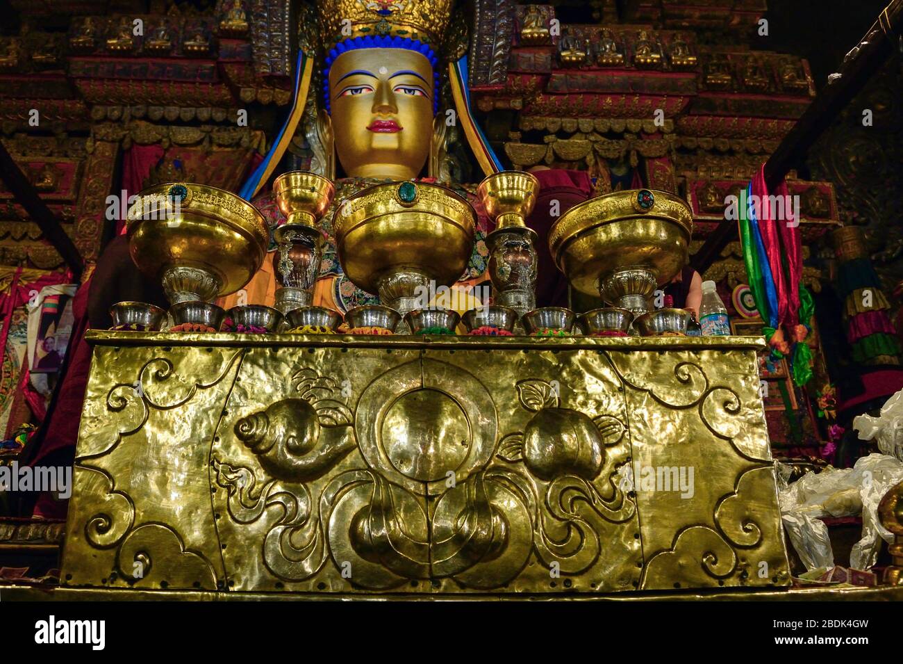An alter before a golden Buddha is carefully adorned with ornate bowls and chalices for offerings at Pelkor Chode Monastery in Gyantsein the autonomou Stock Photo