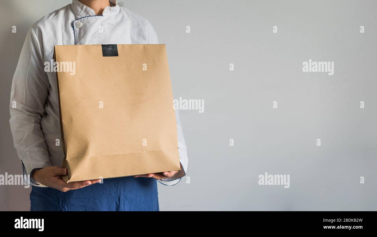 Chef making a delivery of food takeaway in a paper carton bag with copy space. Stock Photo