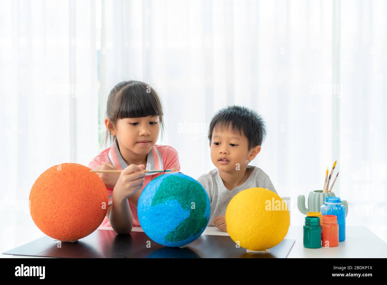 Asian preschool schoolboy with older sibling sister helping and interacting doing painting the earth learning about the solar system at home, Homescho Stock Photo