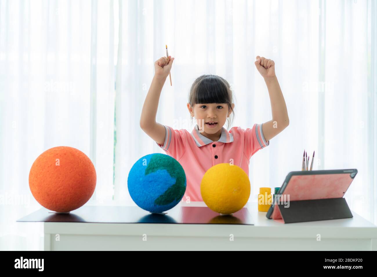 Asian elementary schoolgirl arm raises to sucess painting solar system model learning about the solar system via video conference with teacher at home Stock Photo