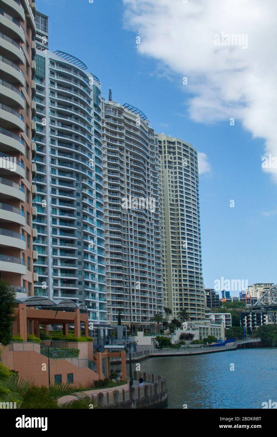 Modern high rise buildings, inner city riverside apartment blocks, rising into blue sky & towering over calm water of river in Brisbane Australia Stock Photo