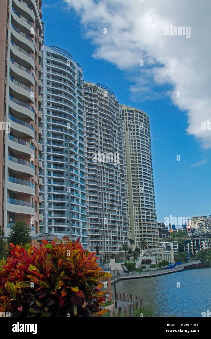 Modern high rise buildings, inner city riverside apartment blocks, rising into blue sky & towering over calm water of river in Brisbane Australia Stock Photo