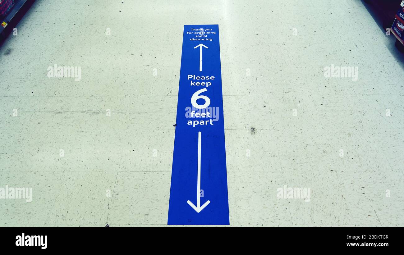 Blue sign on the floor of a supermarket asking customers to stay at least 6 feet apart to prevent the spread of coronavirus. Stock Photo