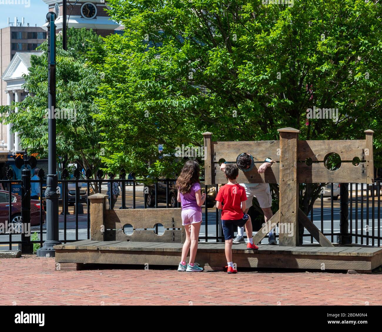 Two children, a boy, and a girl standing before a man in stocks in the courtyard of the Old State House, downtown Hartford CT Stock Photo