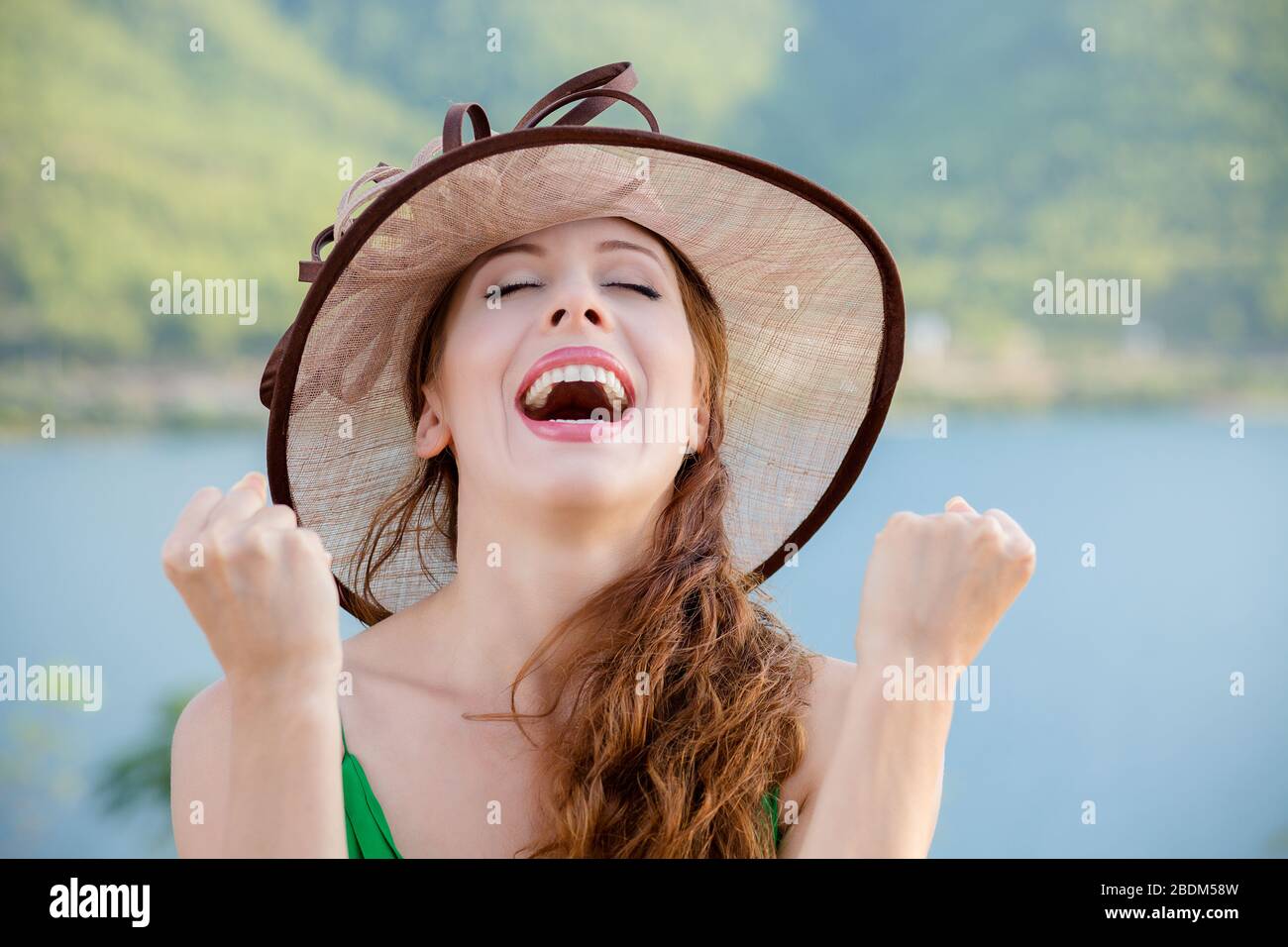 Lucky girl. Happy young woman happy exults pumping fists ecstatic isolated green wall background. Celebrate success concept. Lady in hat by the sea. F Stock Photo