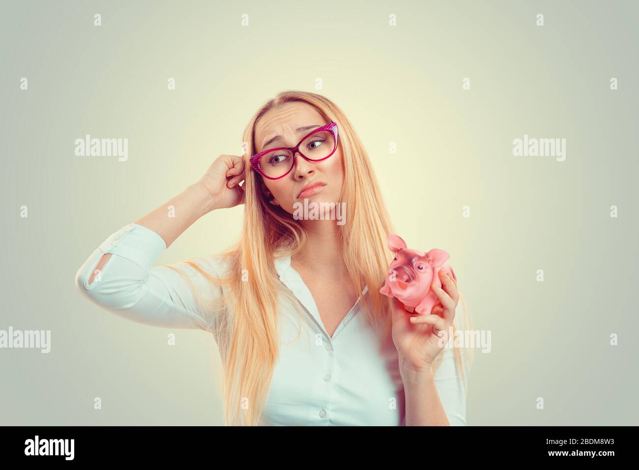 Closeup portrait stressed young woman looking at piggy bank thinking ...