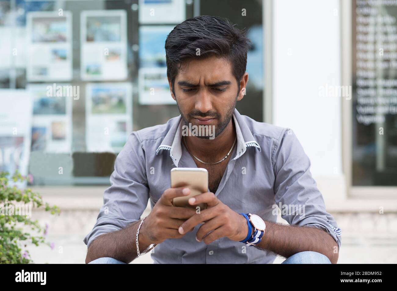 Man phone. Closeup portrait angry indian male holding texting looking at cellphone isolated outdoors background Stock Photo