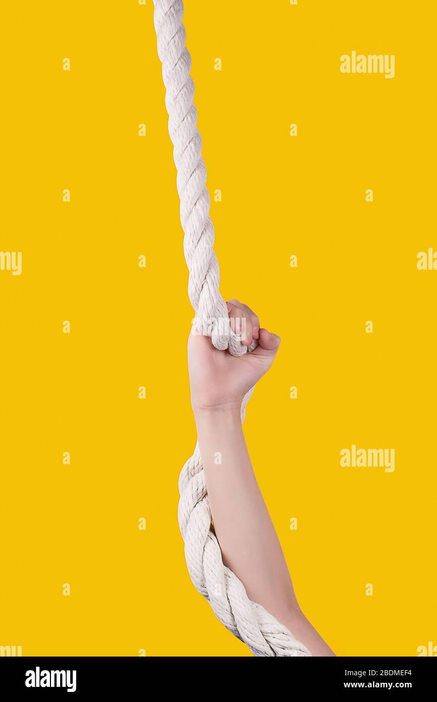 Kid's hand on white rope on vivid yellow background. Child resistance. Work hard and make efforts concept. Child's hand holding the rope. Stock Photo