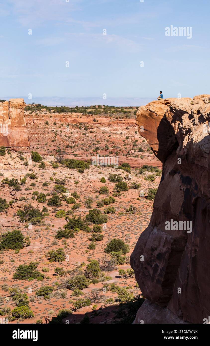 A man sitting relaxed at the top of a sheer drop off, Canyon Lands National Park, Utah, USA. Stock Photo