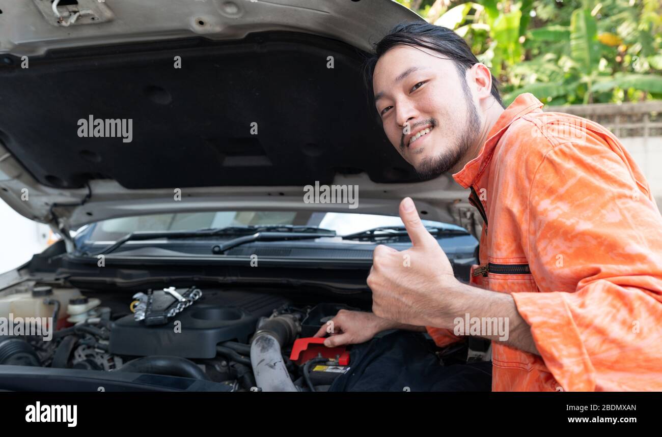 The mechanic in an orange dress uniform opened the car bonnet and  discovered an abnormality preventing the car to start. The concept of  offsite soluti Stock Photo - Alamy