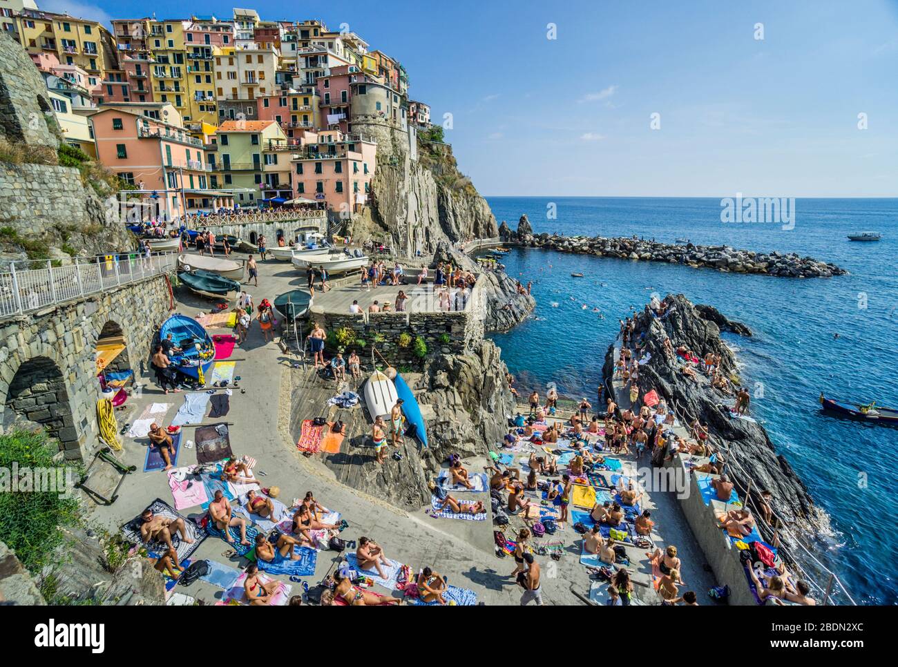 sun seekers at the rock fringed harbour of Manarola in the Cinque Terre, Ligurian Riviera di Levante, Liguria, Italy Stock Photo