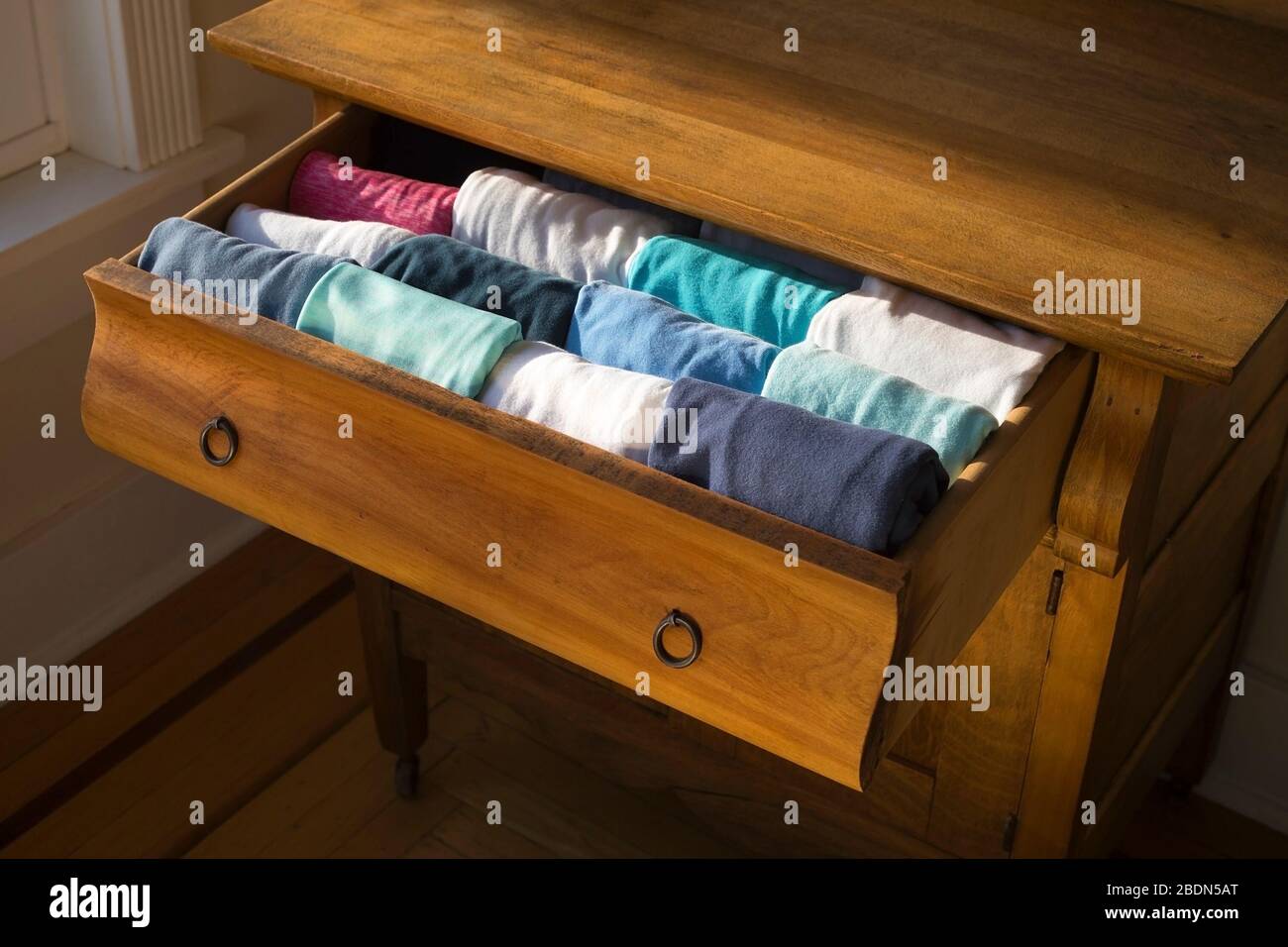Woman's shirts in an antique wood bureau drawer folded in the KonMari method of home organization expert Marie Kondo. Stock Photo