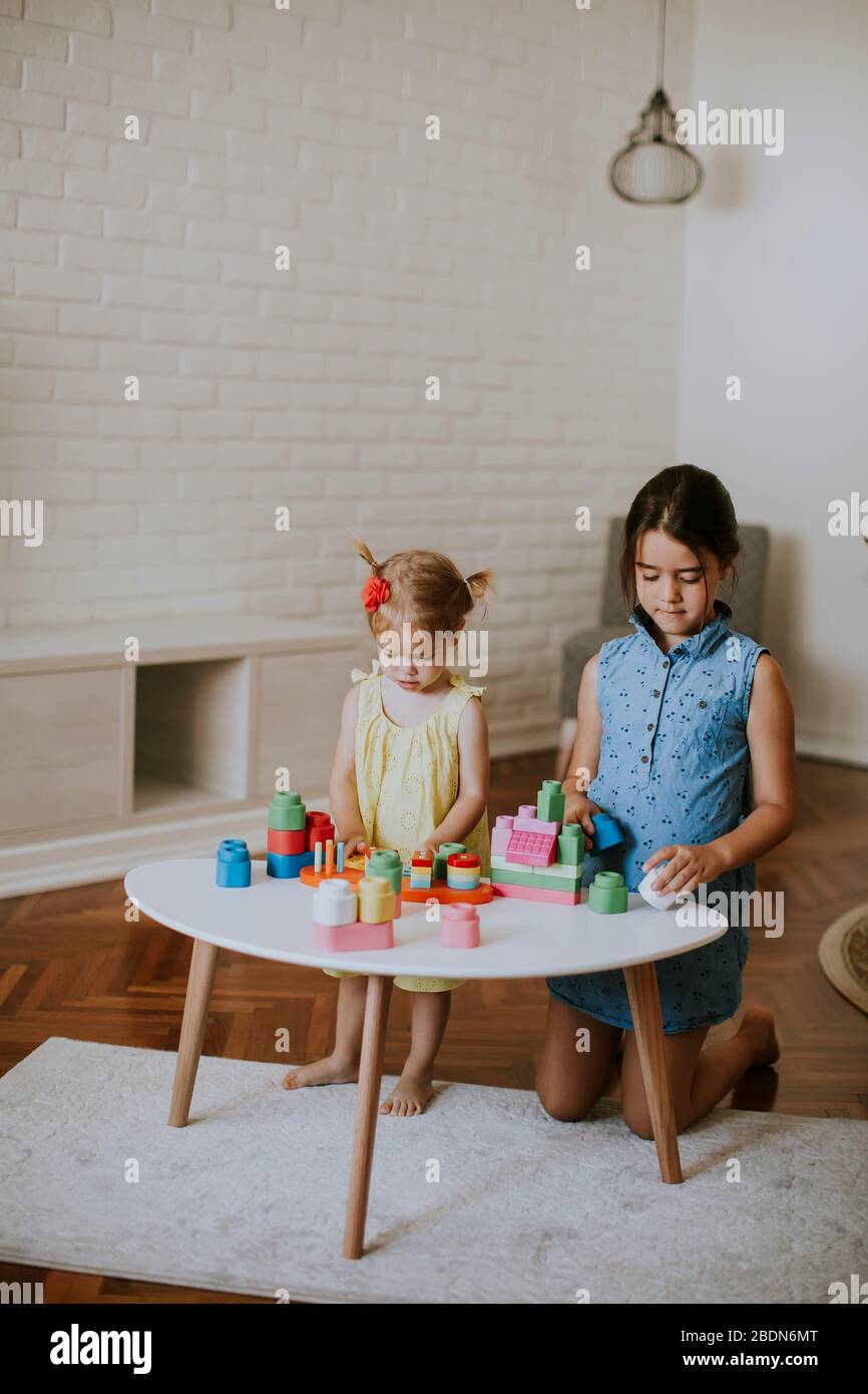 Two cute little girls play with blocks at the table in the room Stock ...