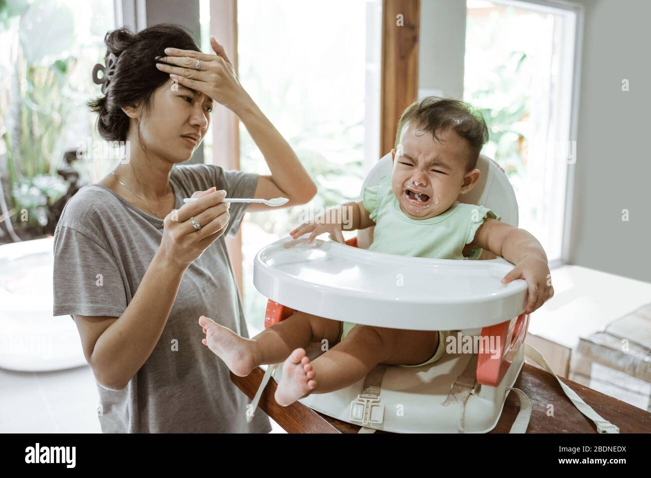 stress mother while feeding her baby at home Stock Photo