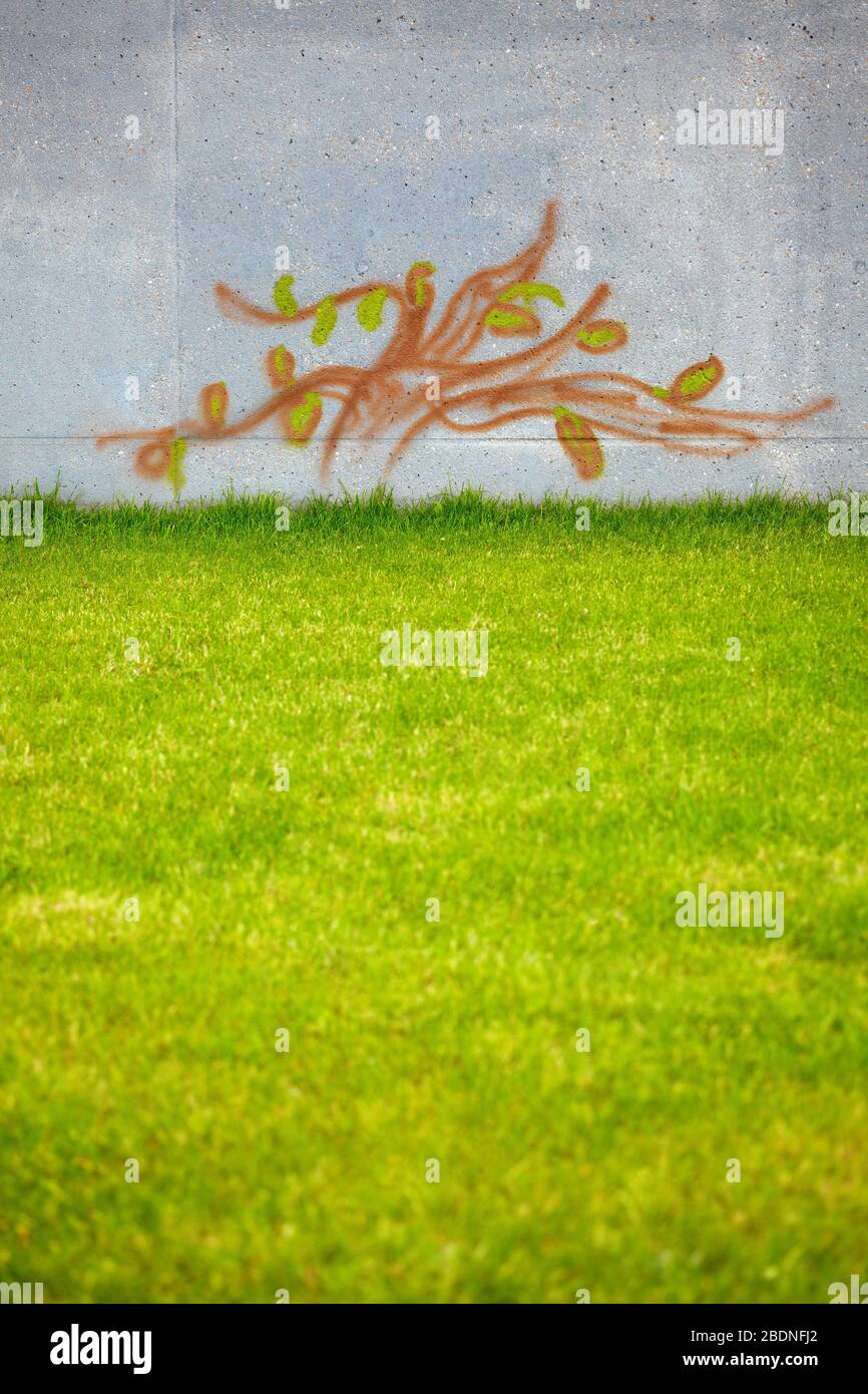 Tree as a graffito on a wall next to a green meadow Stock Photo