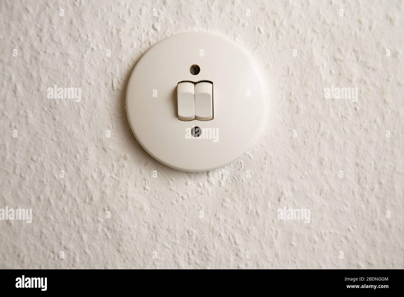Round light switch on wall with white wallpaper Stock Photo